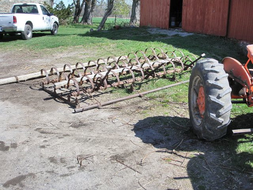 A harrow: a piece of agricultural equipment drawn behind a tractor and used to scrape across and break up the soil after ploughing.