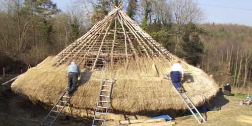 The roof of a reproduction Iron Age round house at the Chiltern Open Air Museum, in the process of being thatched. The roof has a conical shape made of stakes arranged in a circle and bound together at the apex. Horizontal laths are added in concentric circles, and then thatch is fixed all round the outside.