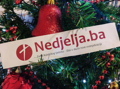 Close-up of view of a banner for the Bosnian Catholic website Nedjelja.ba nestling in an artificial Christmas tree decorated with shiny red decorations.